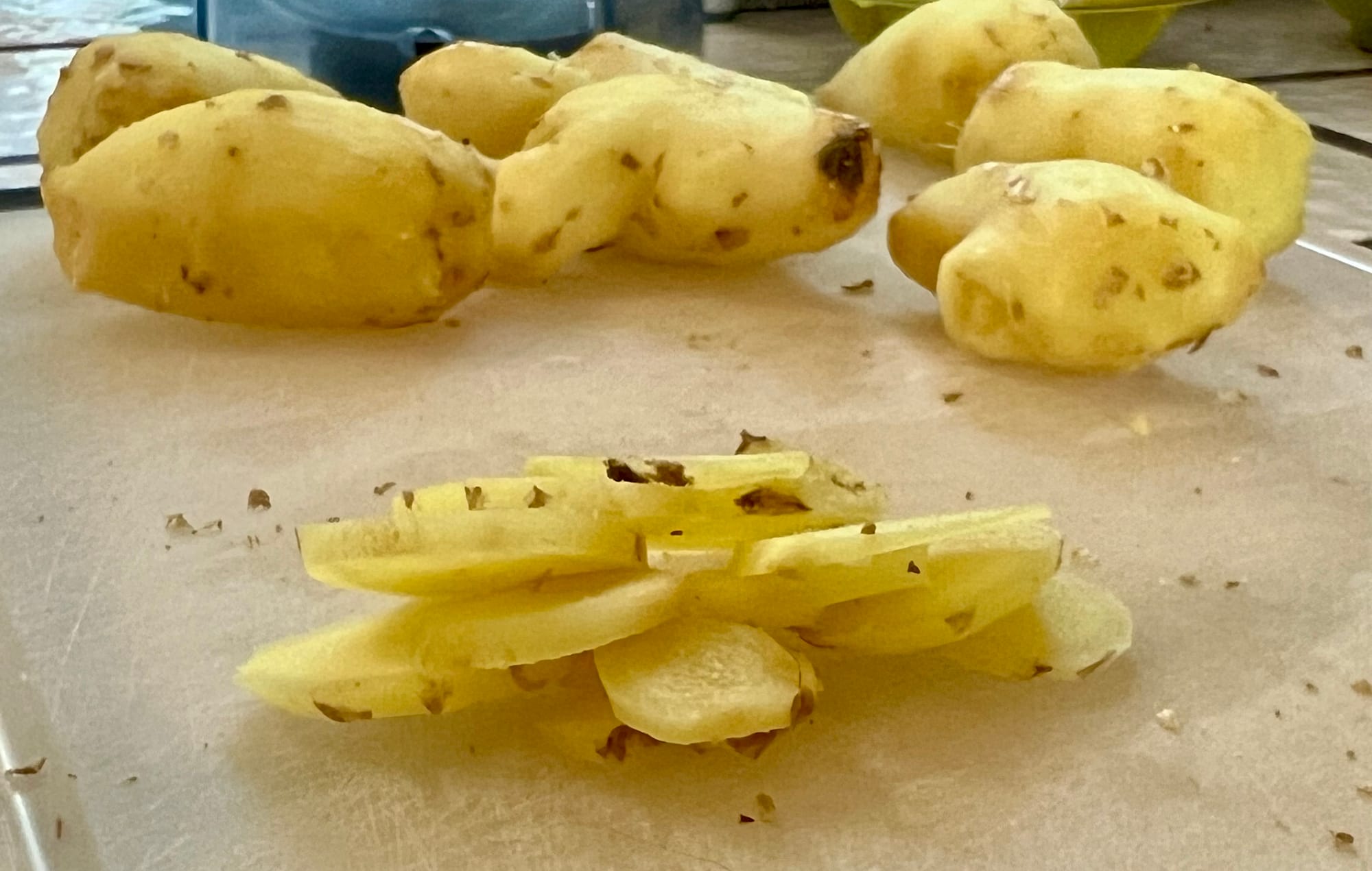 A pile of thin ginger slices is in front of several hunks of unsliced ginger.