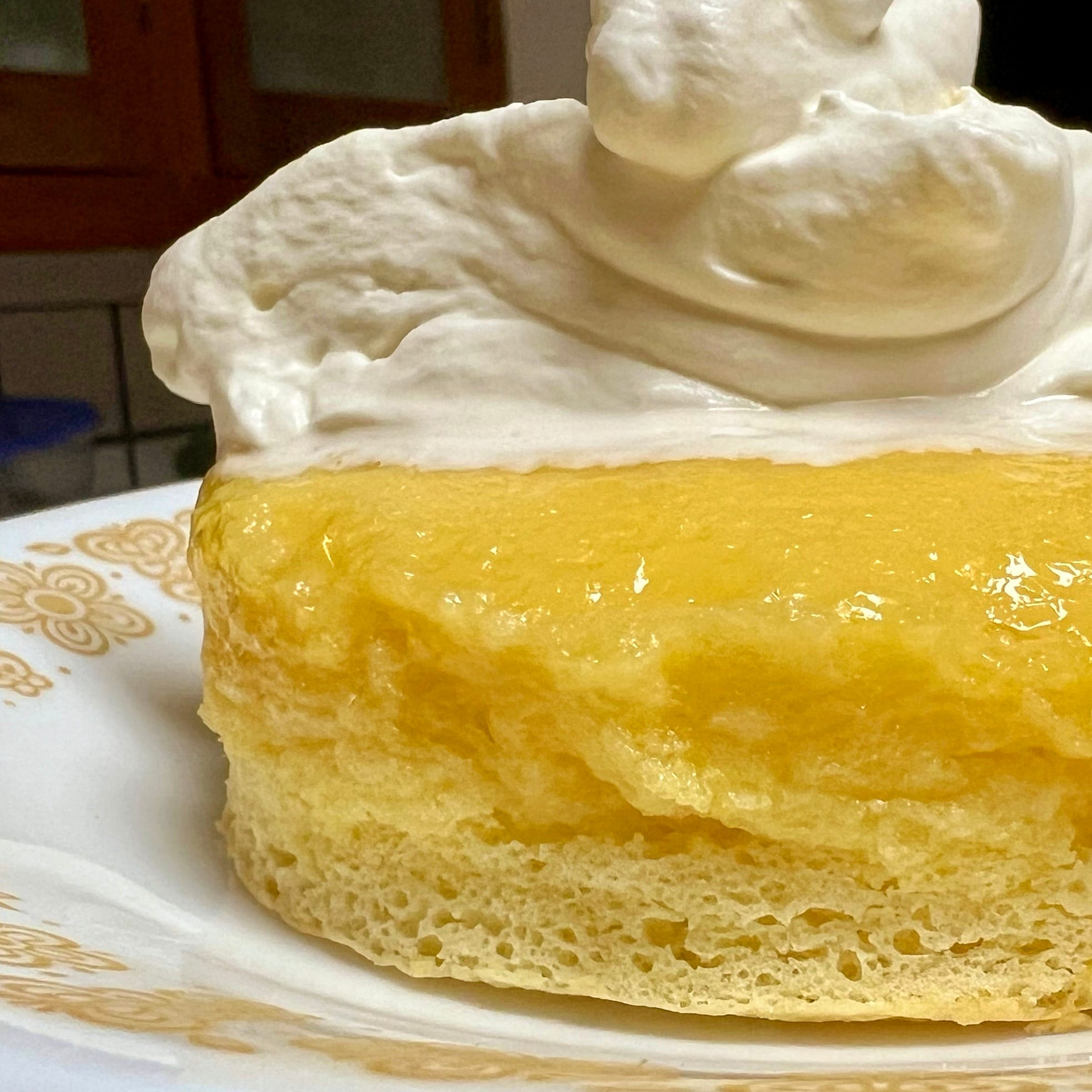 Close up of a pale yellow cake, topped with a thick yellow custard, topped with whipped cream.