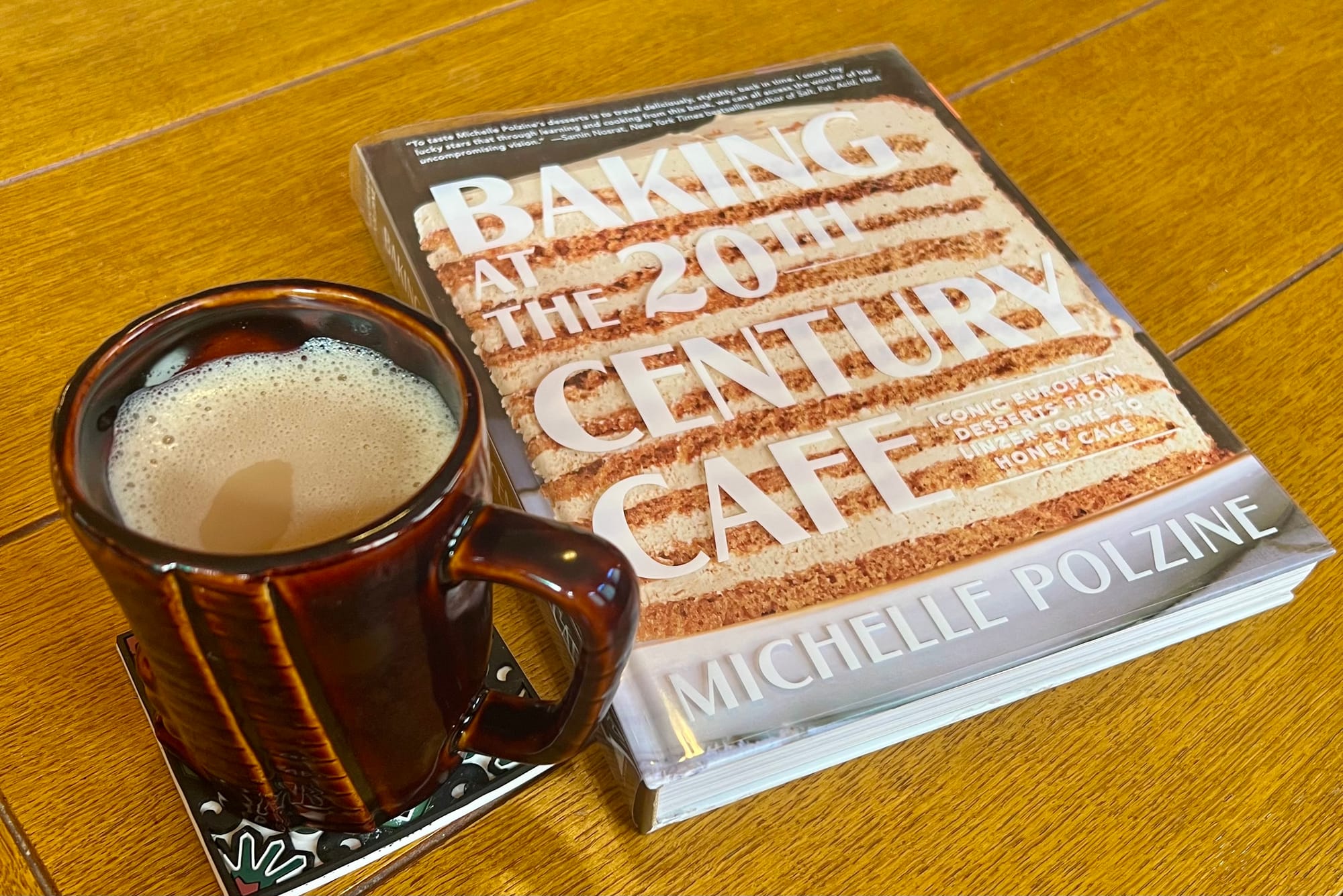 A cookbook, Baking at the 20th Century Cafe by Michelle Polzine, alongside a mug of coffee.