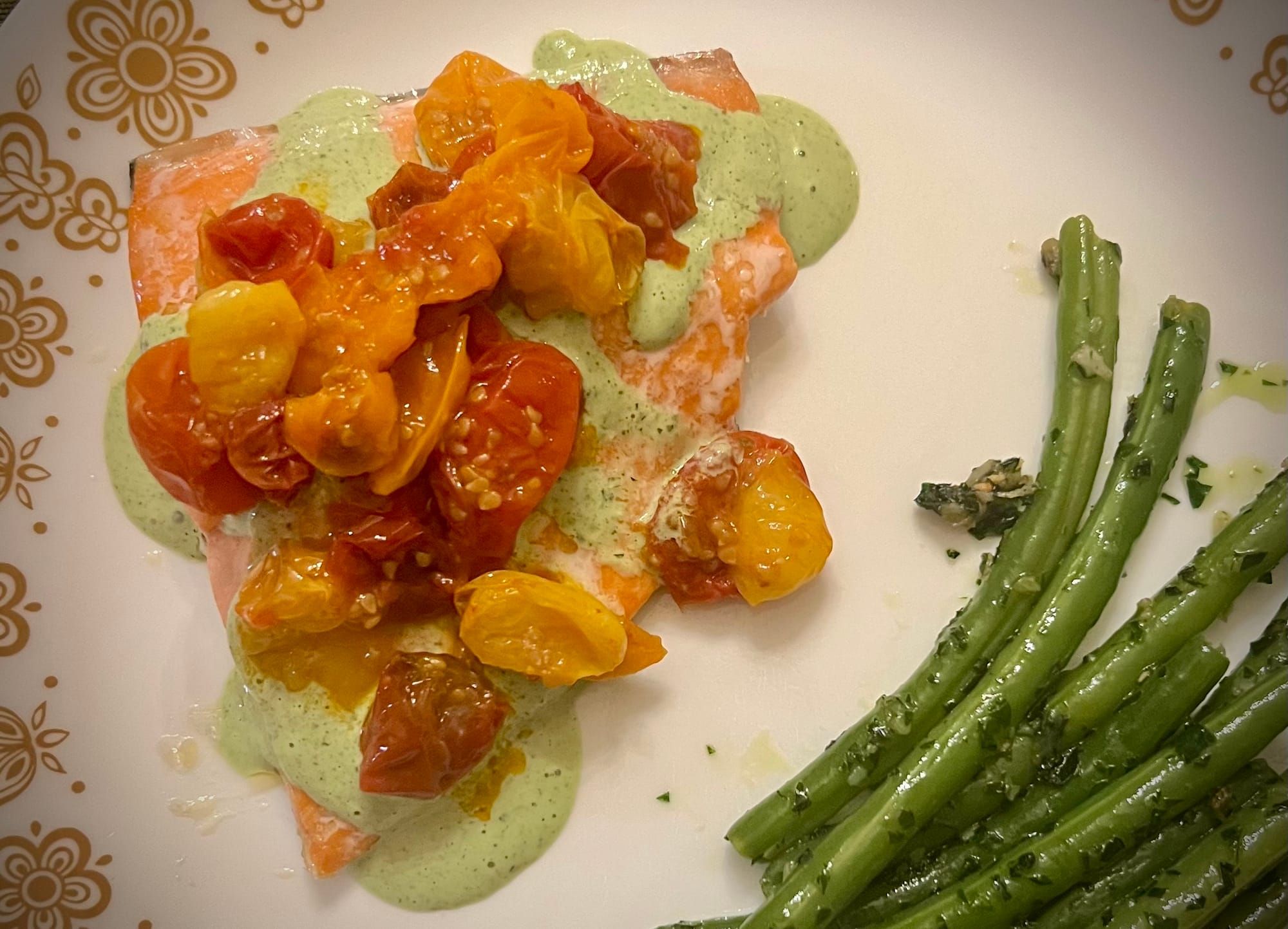 A triangular filet of pink salmon is topped with pale green sauce and roasted cherry tomatoes.