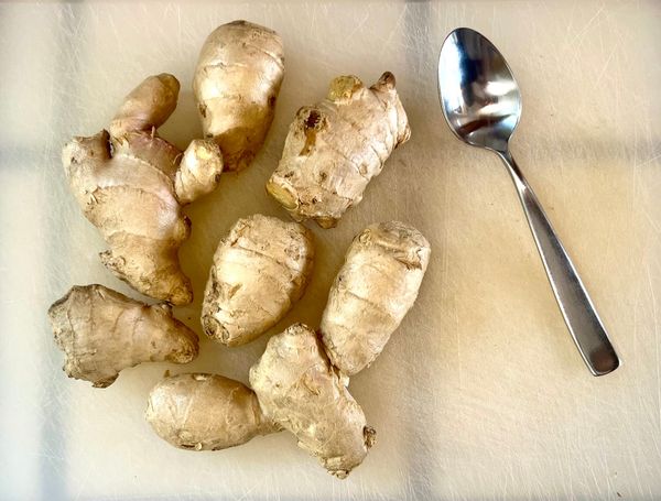 Large pieces of ginger root, alongside a silver spoon on a cutting boar