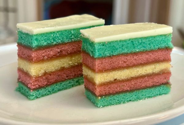 Two cookies stand upright on a plate. They're shaped and colored just like the transgender flag, with blue, pink, and white layers.