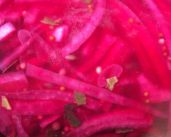 Bright pink pickled red onions are seen in their brine, along with pickling spices.