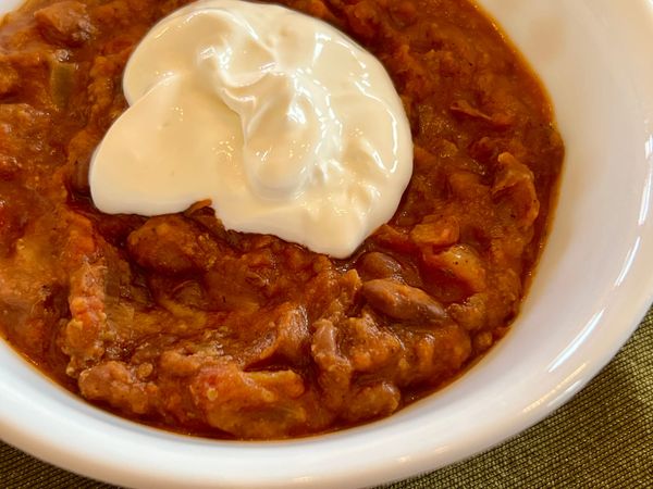 Chili is seen in a bowl, topped with sour cream.