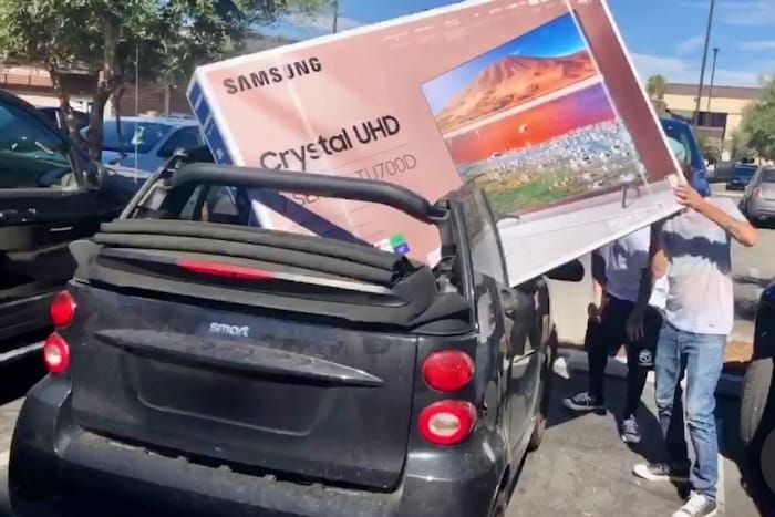 People trying to load a 65 inch tv into a smart car. The tv is 25% wider than the car. They are trying to put it in the back seat with the top down. They look dumb. 