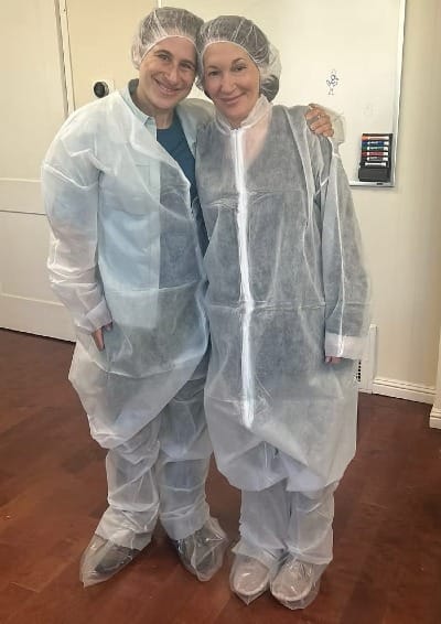 Hanna and Alison smiling in full disposable protective gear including hairnets, gowns, and shoe covers during a facility tour