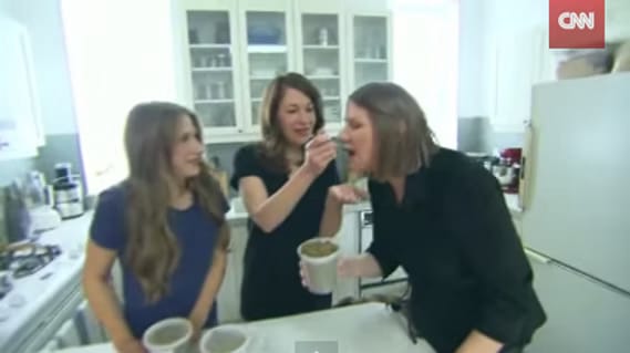 A screenshot of a CNN segment that shows Hanna, Alison, and the CNN reporter Jeanne Moos in a home kitchen where Alison is feeding Jeanne Moos a spoonful of Evermore