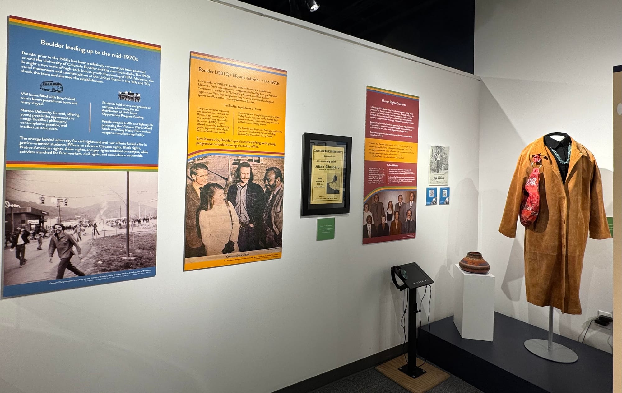 Posters show photos and events from the early 1970s. A jacket, purse, and necklace belonging to Clela Rorex hang on a stand. 