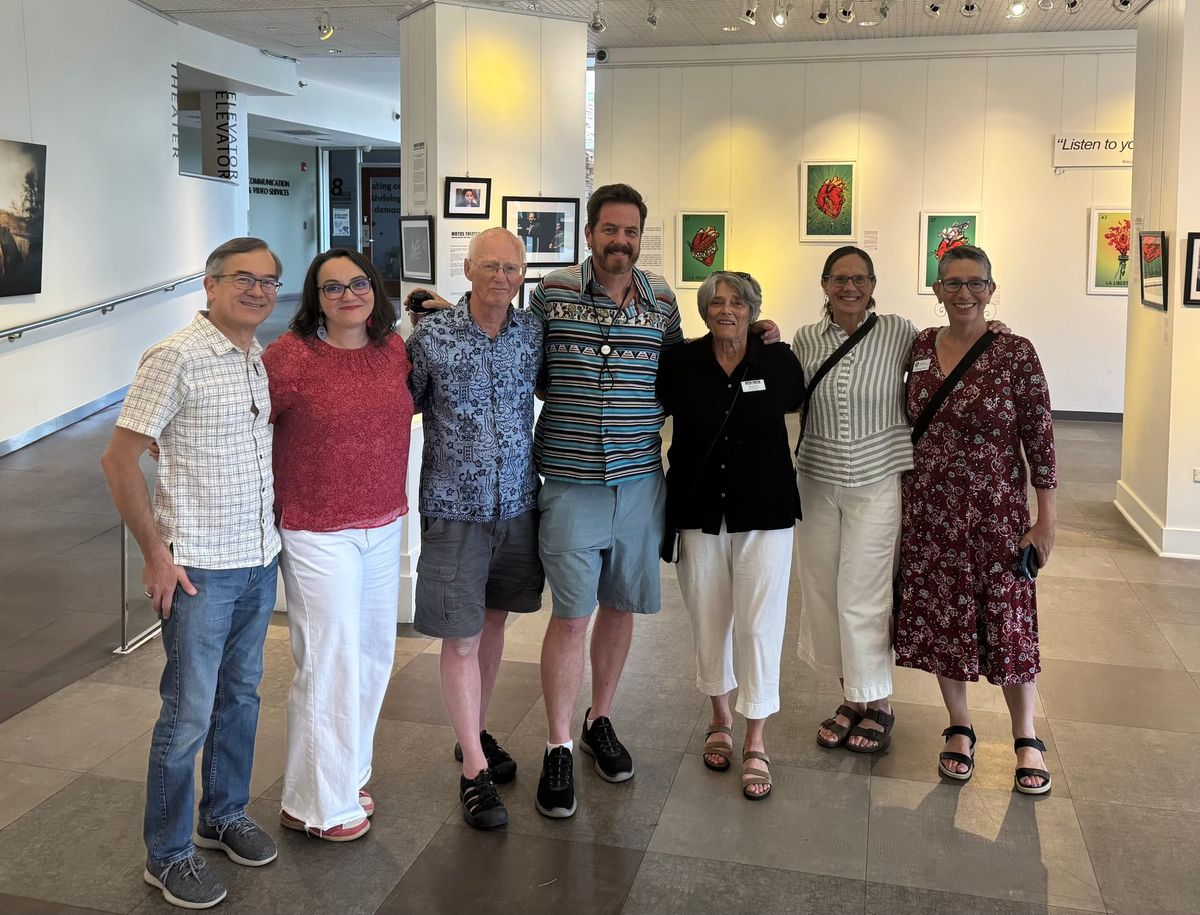 Seven people pose in a modern art gallery with framed artwork on the wall behind them.