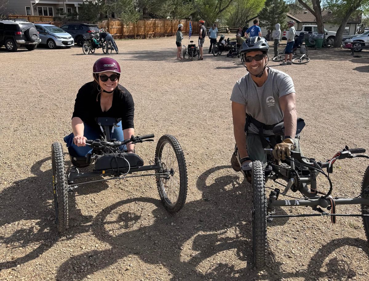 Two participants on adaptive hand bikes in a gravel parking lot at Wonderland Lake.