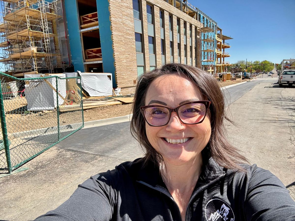 Nicole takes a selfie in front of a construction site. The new building is framed by scaffolding and fencing.