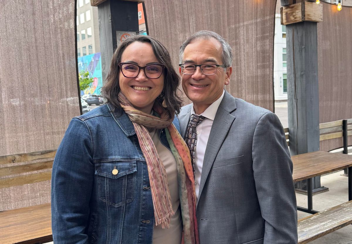Nicole and Art smile at a post-award party. Art wears a gray suit and tie; Nicole wears a denim jacket and scarf.