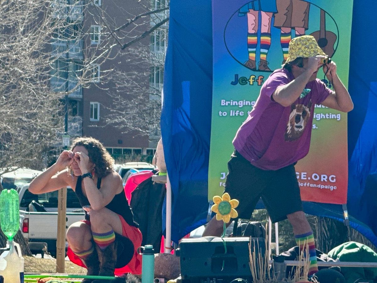 A woman and a man wearing rainbow socks look through binoculars on an outdoor stage.