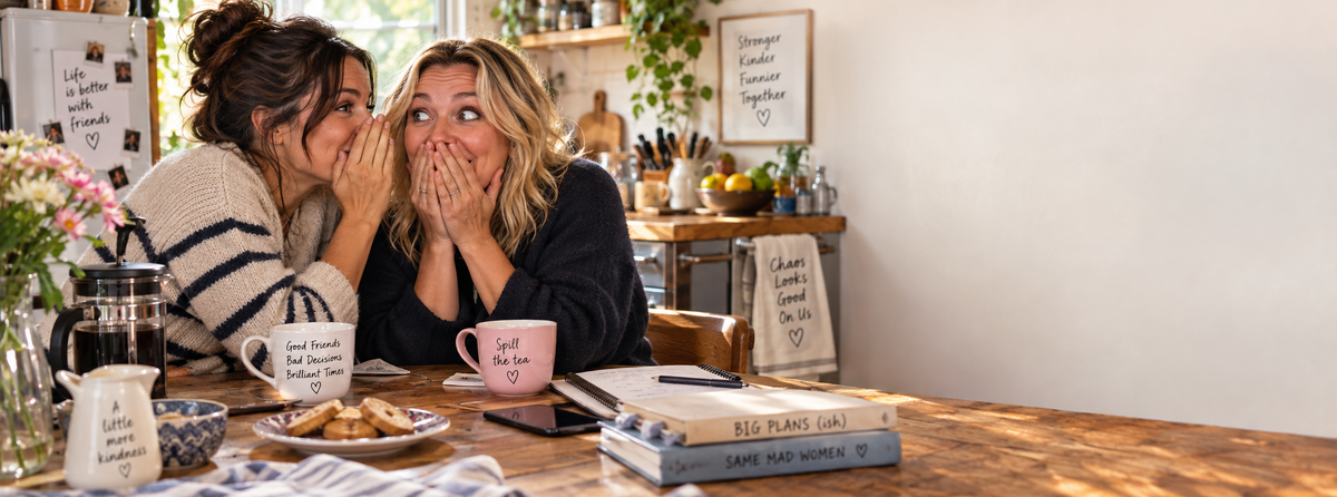 Two friends sharing a secret over coffee and biscuits at a kitchen table