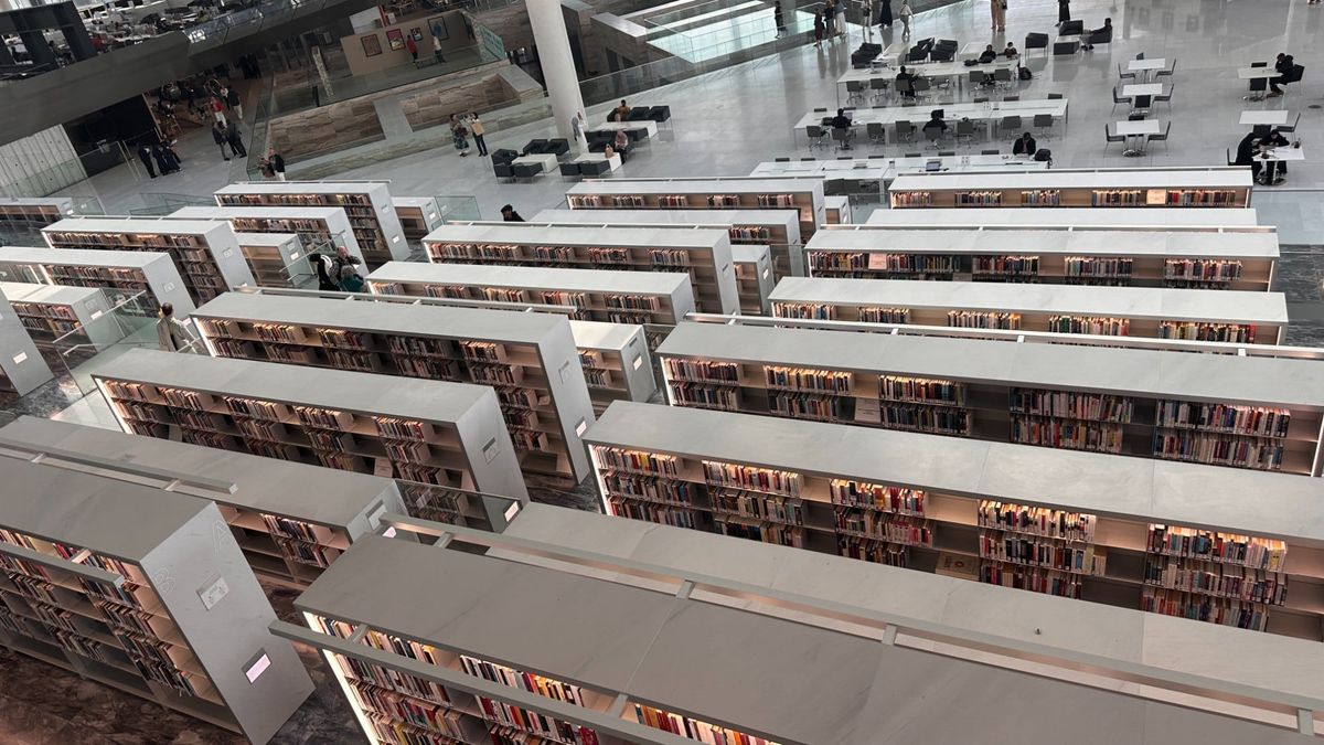 Interior of the Qatar National Library in Doha: tiers of pale shelving and reading terraces under a wide, light-filled roof
