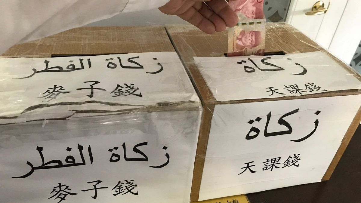 Two cardboard collection boxes in the Taipei Grand Mosque labelled for zakat and zakat al-fitr in Arabic and Chinese, with a banknote being dropped into one