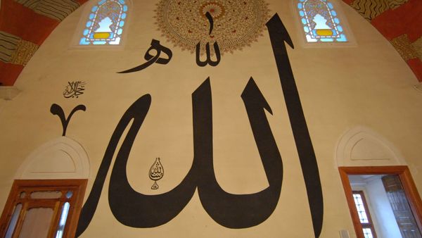 The name of God painted in large black calligraphy on a pale wall of the Old Mosque in Edirne, Turkey