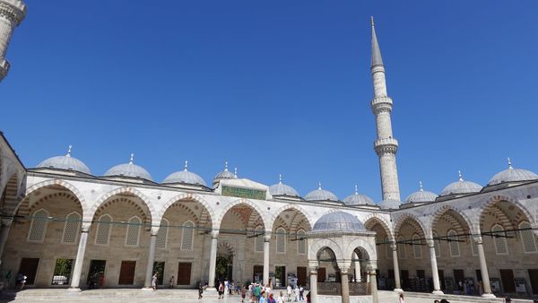 The arcaded courtyard of the Sultan Ahmed Mosque in Istanbul, with a minaret against a clear blue sky