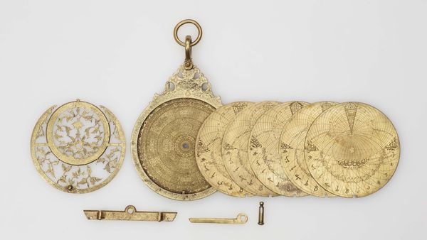 A brass planispheric astrolabe with its interchangeable plates laid out beside it, Khalili Collection of Islamic Art