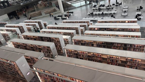 Interior of the Qatar National Library in Doha: tiers of pale shelving and reading terraces under a wide, light-filled roof