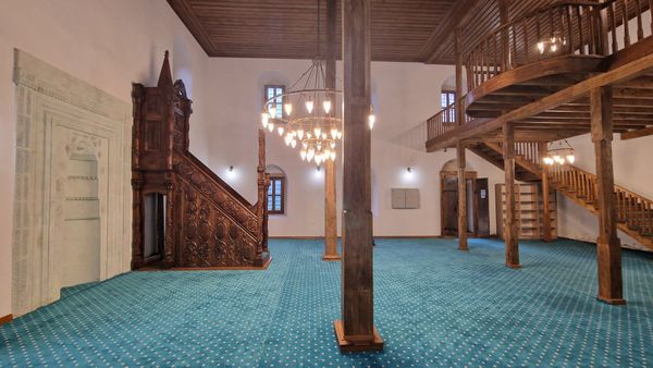 Interior of the historic mosque at Sıraağaç, Trabzon, with its carved wooden minbar and the wooden upper gallery (mahfil) above the prayer hall
