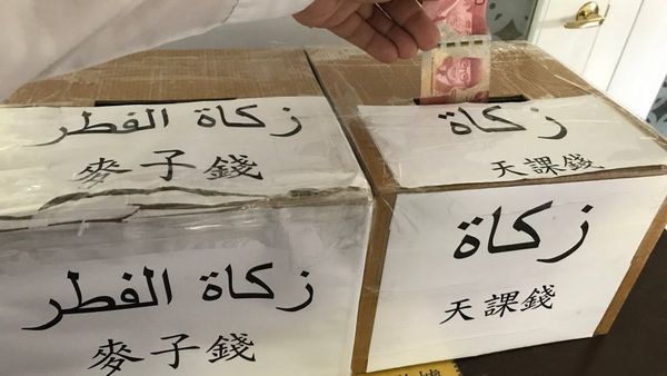 Two cardboard collection boxes in the Taipei Grand Mosque labelled for zakat and zakat al-fitr in Arabic and Chinese, with a banknote being dropped into one
