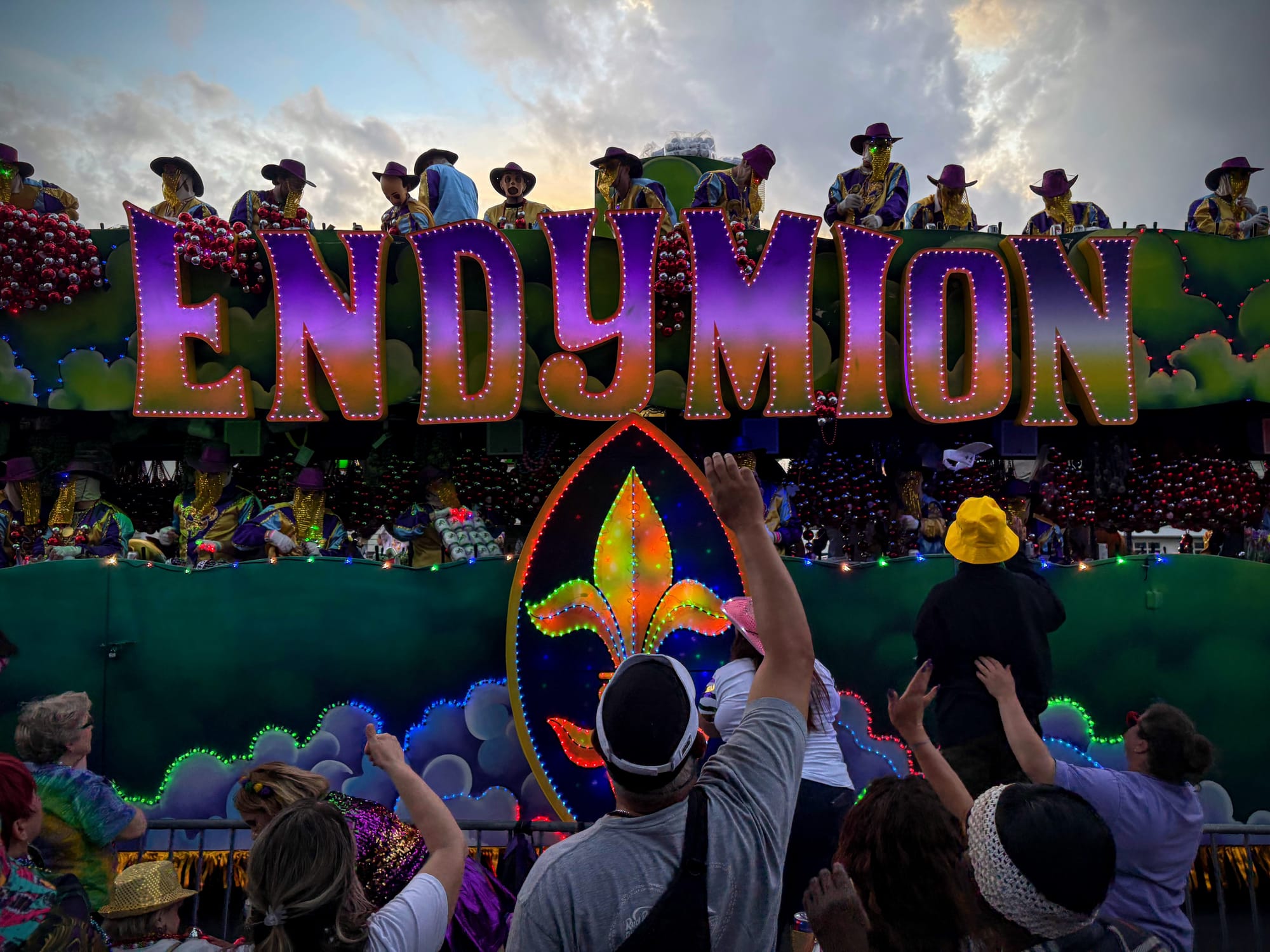 arms are raised for throws as a float with ENDYMION on its side rolls past