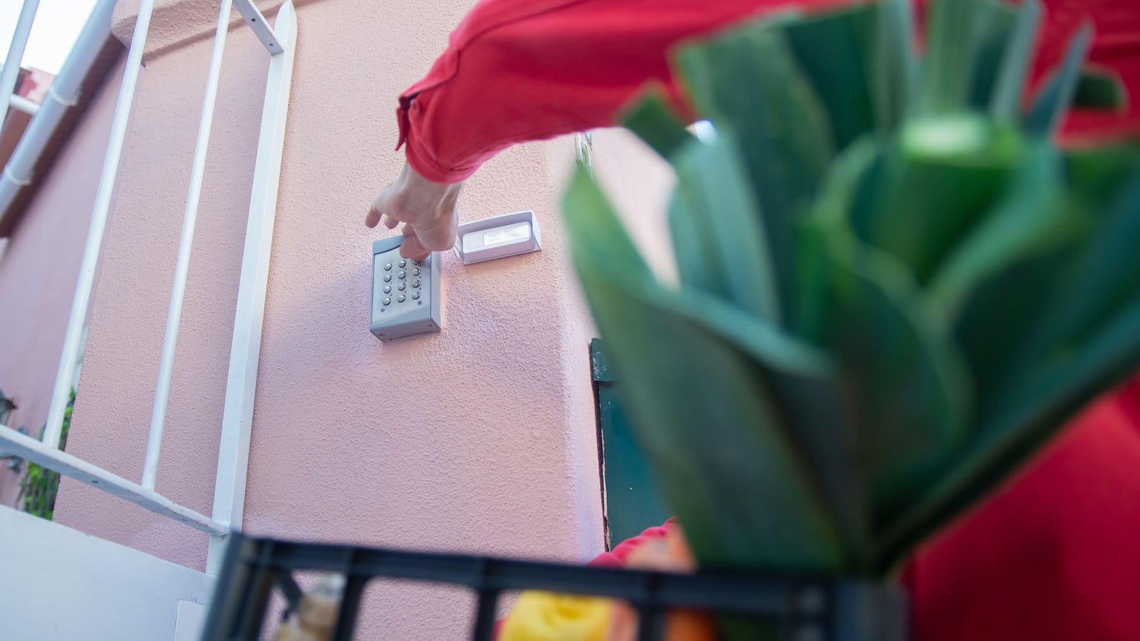 Person carrying groceries enters a door code on a wall-mounted keypad beside a green door