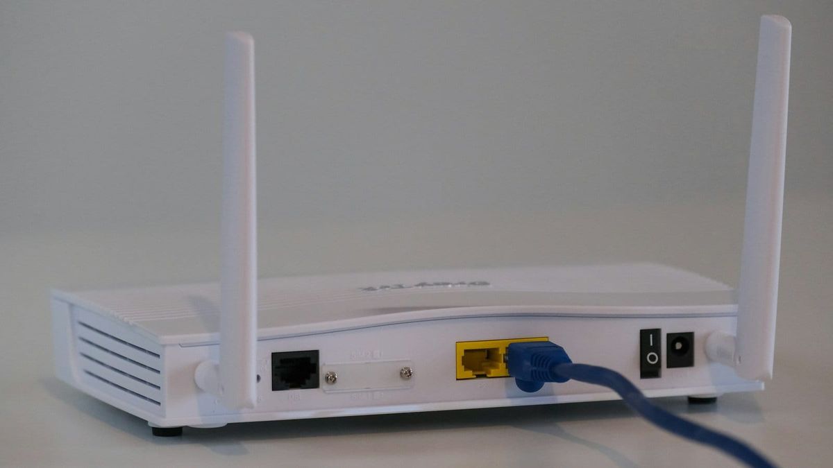 Back of a white Wi-Fi router with a blue Ethernet cable plugged into its network port