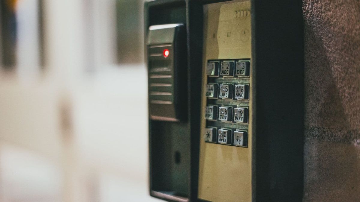 Wall-mounted access keypad and proximity card reader with a red status light on an exterior stone wall