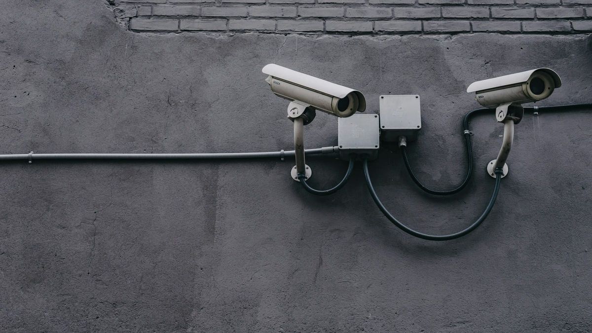 Two outdoor bullet security cameras mounted on a gray exterior wall with wiring run through conduit