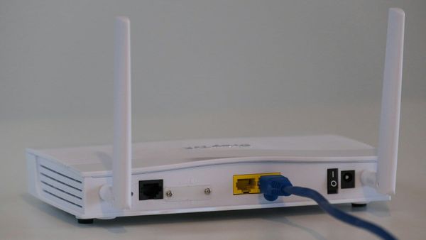Back of a white Wi-Fi router with a blue Ethernet cable plugged into its network port