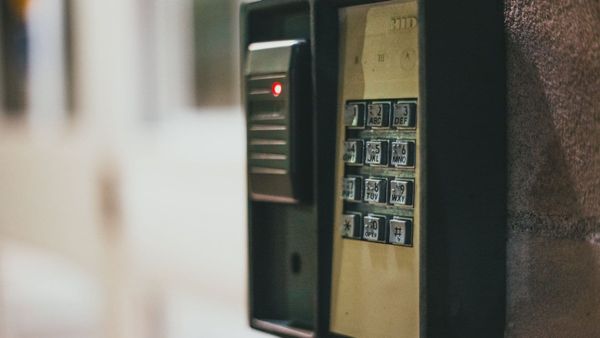 Wall-mounted access keypad and proximity card reader with a red status light on an exterior stone wall