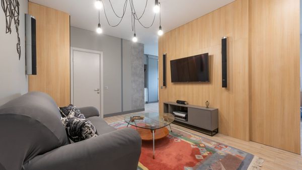 Modern living room with slim tower speakers mounted on a wood accent wall on either side of a wall-mounted TV