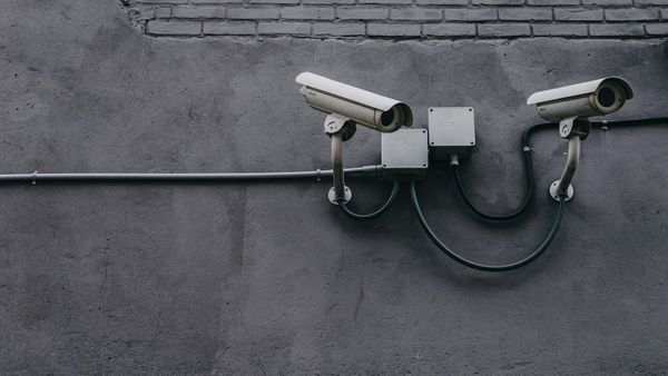 Two outdoor bullet security cameras mounted on a gray exterior wall with wiring run through conduit