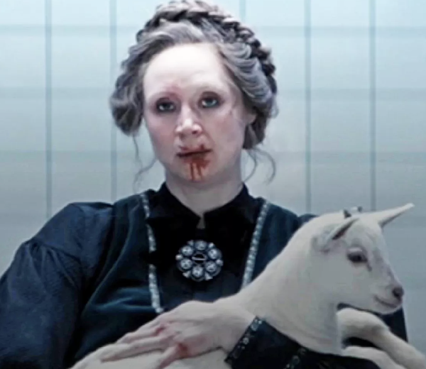 screen shot of blonde woman with blood on her face holding a baby goat