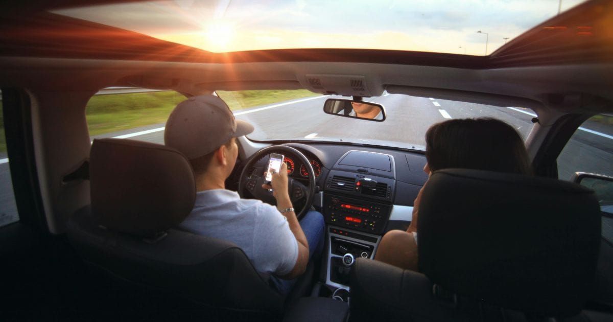 Couple driving together at sunset, driver holding phone on long road trip