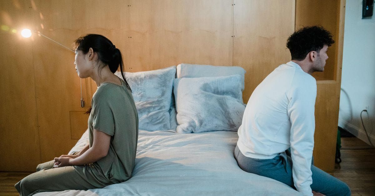 Couple sitting back to back on bed looking in opposite directions