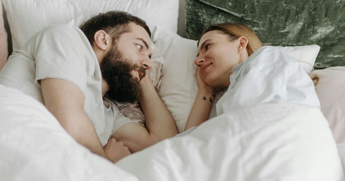 Couple lying in bed facing each other smiling in the morning
