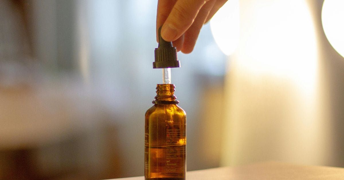 Hand reaching for dropper of amber CBD oil bottle in warm golden bedroom light