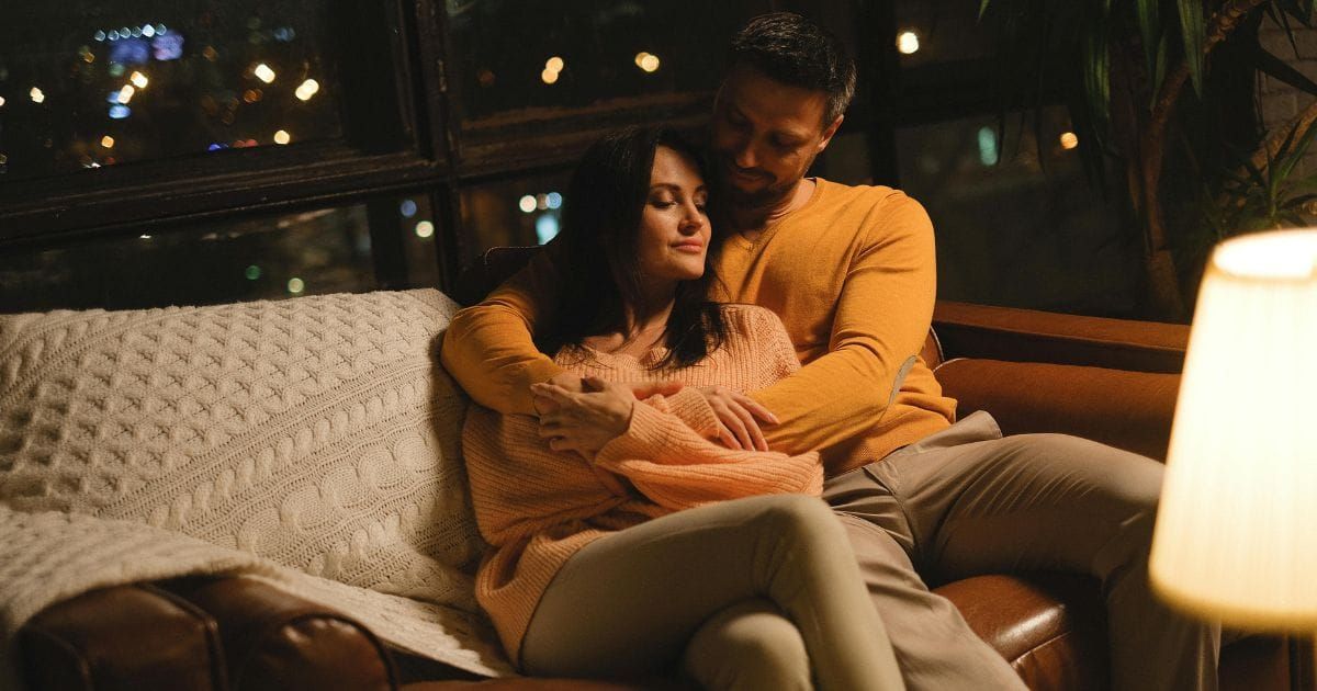 Couple relaxed together on couch in warm evening light woman with eyes closed leaning into partner
