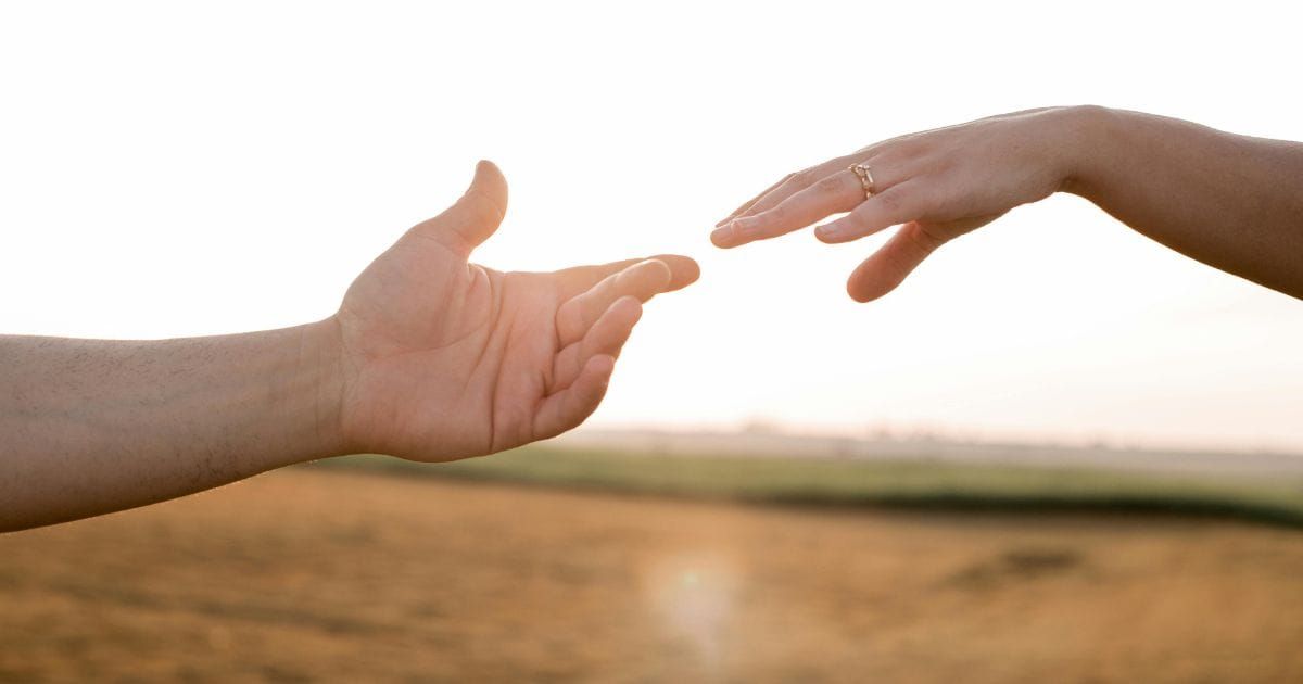 Married couple's hands reaching toward each other but not quite touching in warm golden sunset light