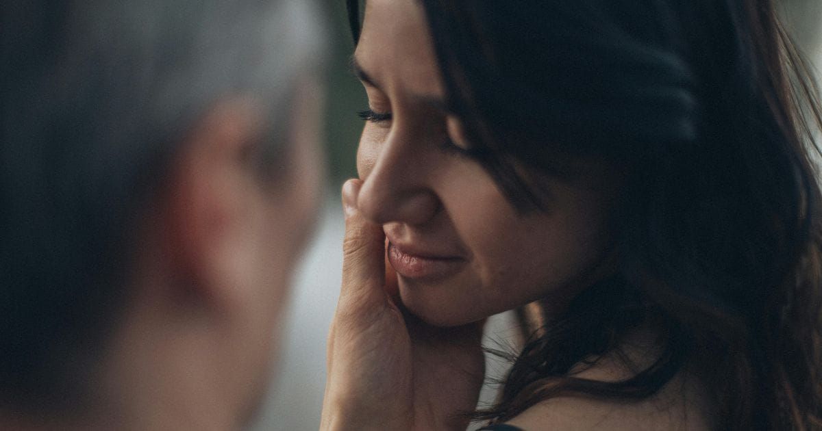 Man tenderly cupping woman's face as she closes her eyes in a moment of trust and vulnerability