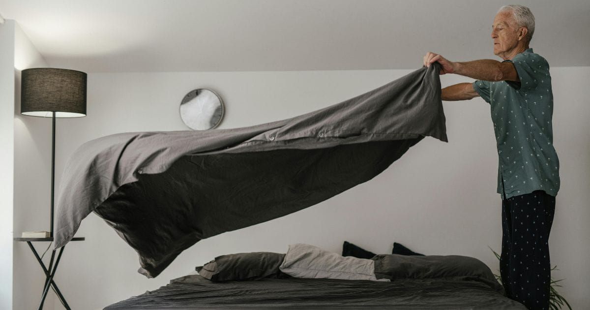 Older man laying out blanket over bed preparing the space with intention and care
