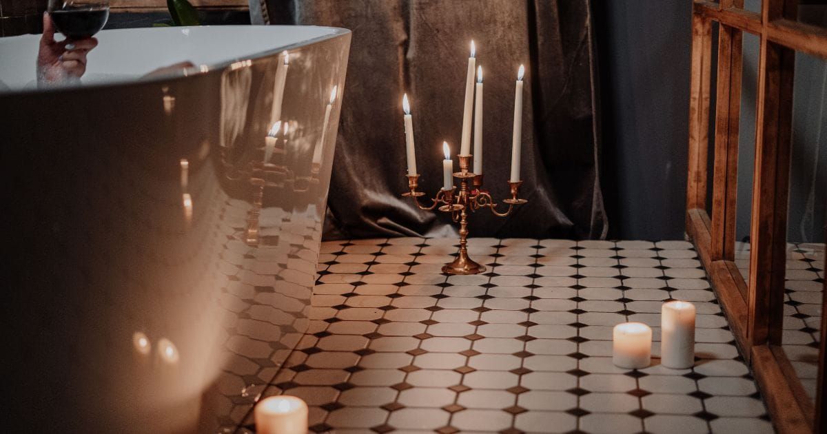 Candelabra and candles glowing on bathroom floor beside a tub at night