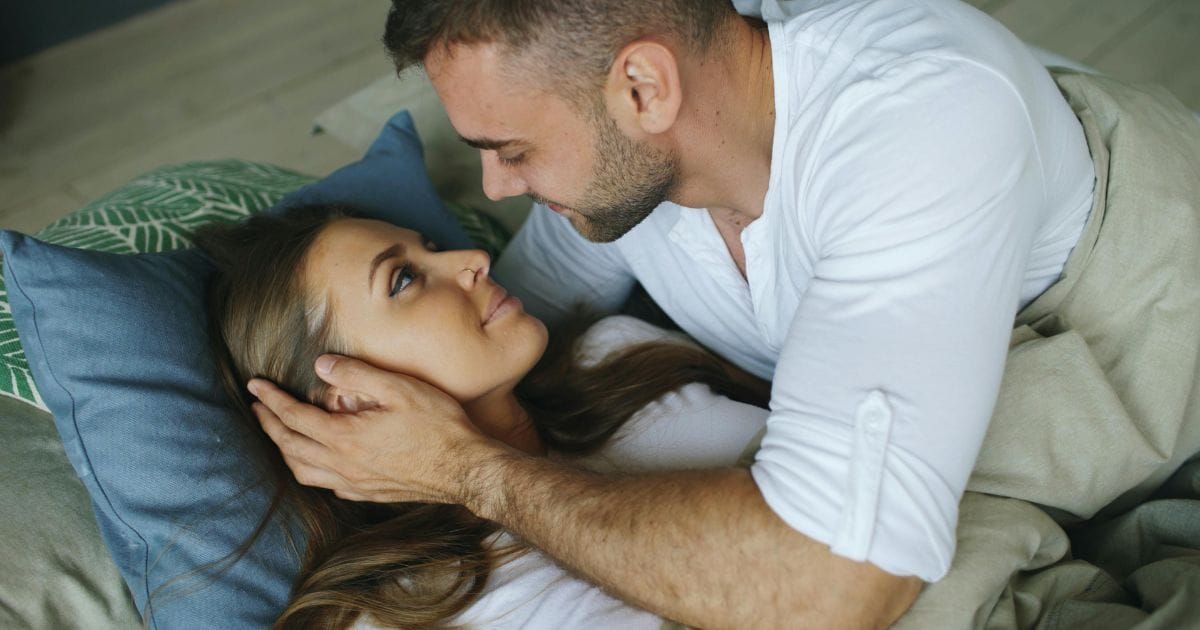 Man tenderly holding woman's face in his hands as they look at each other with trust and intimacy in bed