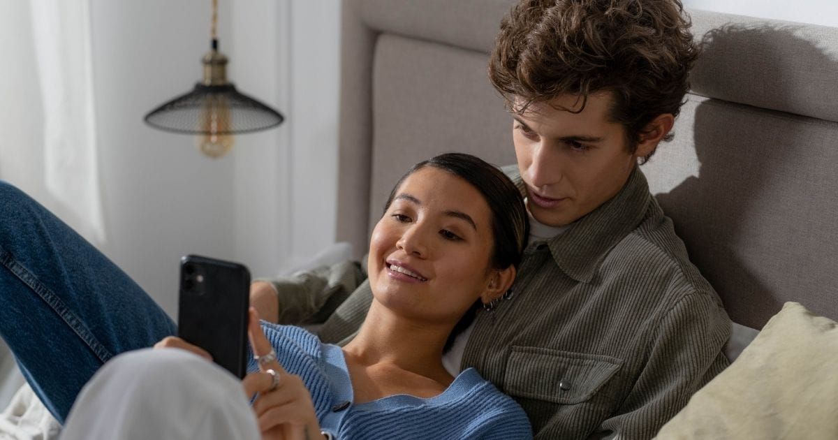 Couple looking at a phone together, smiling, in bed