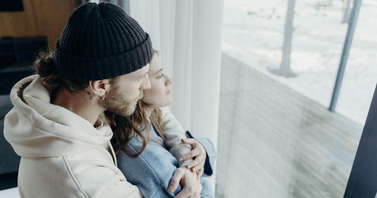 Couple embracing warmly, looking out a window together.