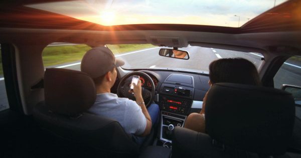 Couple driving together at sunset, driver holding phone on long road trip