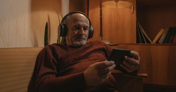Older man sitting alone in evening light absorbed in his phone